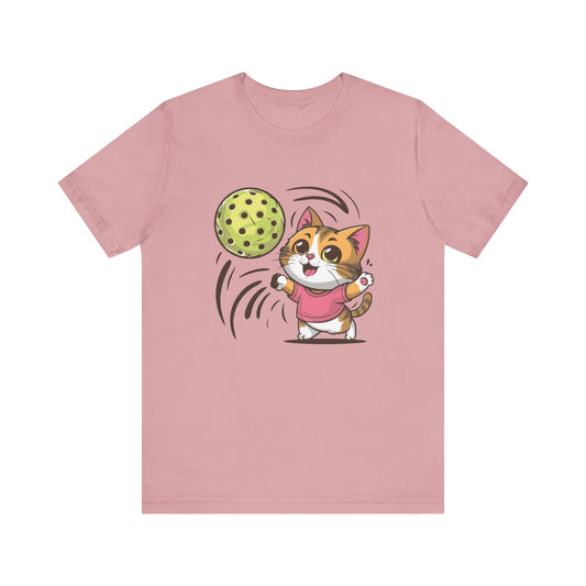 Pink t-shirt featuring an adorable cartoon cat in a pink shirt, joyfully playing with a large pickleball.