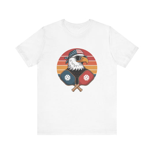 USA Eagle pickleball t-shirt featuring bald eagle head with American flag bandana and crossed pickleball paddles on patriotic emblem